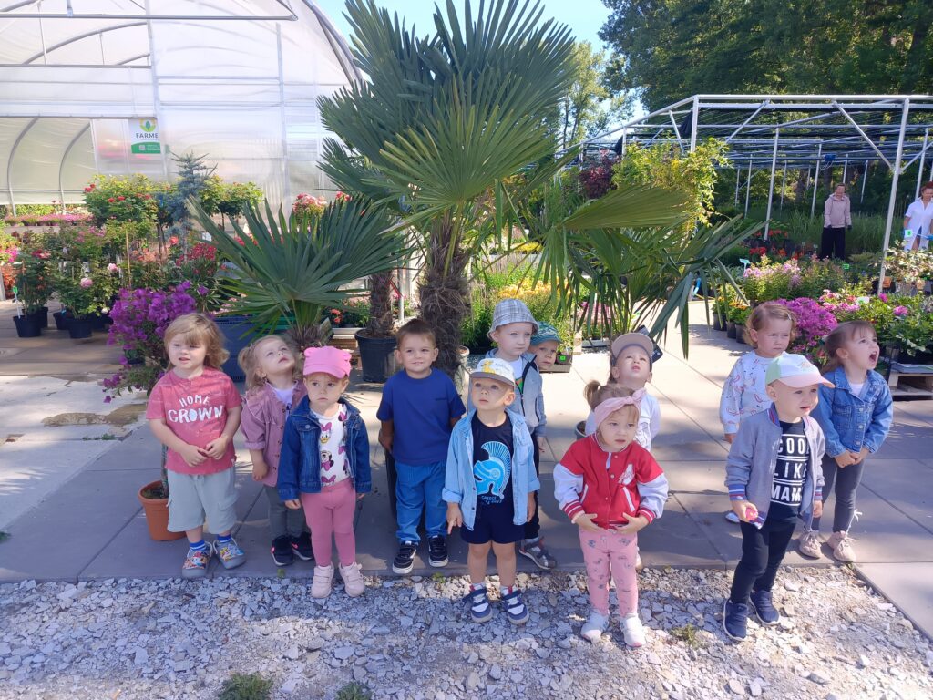 Dzieci stoją pod palmami w doniczkach.